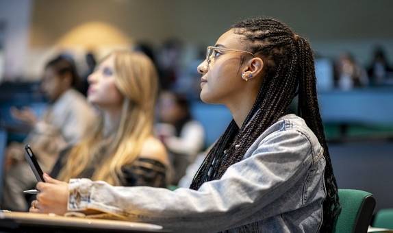 Student with glasses and braided hair sitting at a desk in a lecture theatre