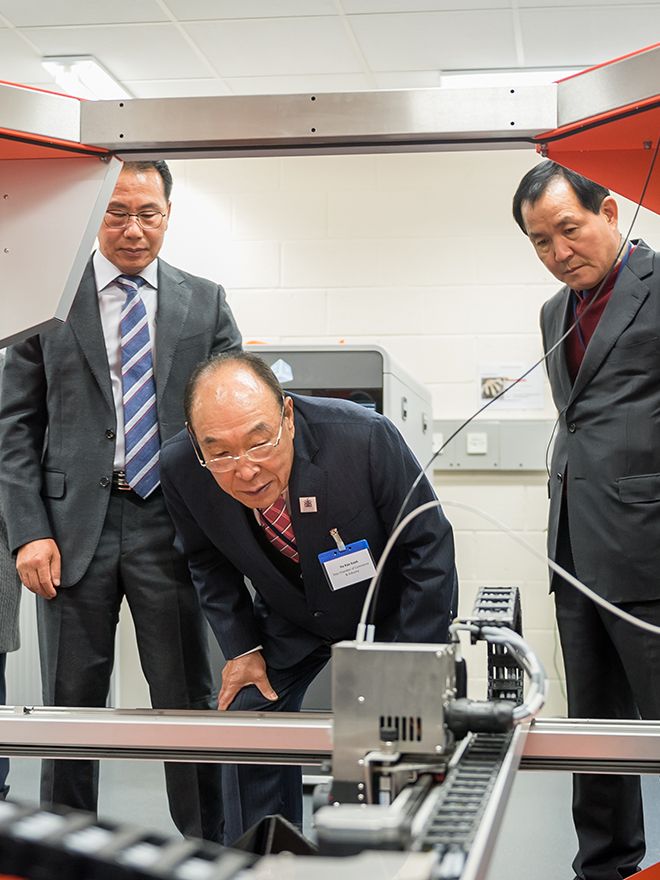 Three men examine a 3D printing machine