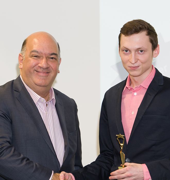 Sam Nozdrachov is presented with a trohpy by Vince Tallent. The two shake hands and hold a trophy.