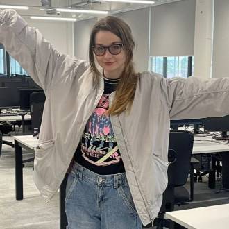 Andrea Lupori, a student in jeans with a KISS t-shirt, wearing glasses, stands with arms outstretched.
