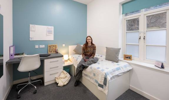 A female student sitting on her bed in the single en suite room type