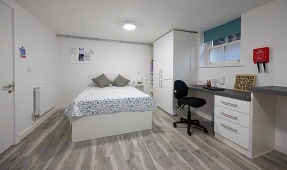 Large self-contained studio showing a double bed, storage cupboards and desk