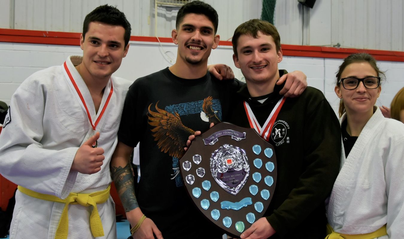 jiu jitsu winners pose with trophy in their martial arts gowns