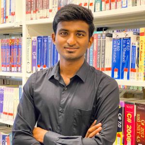 Harish Loganathan, a student from India, stands smiling before bookshelves.