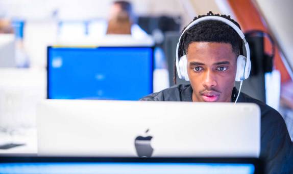 student wearing headphones and working on a Mac