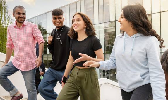 Four smiling students walk outside at near Kingston Business School, Kingston Hill campus