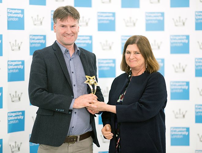 Nigel Page and Clarissa Wilks stand together with trophy in front of Kingston University branded hoarding