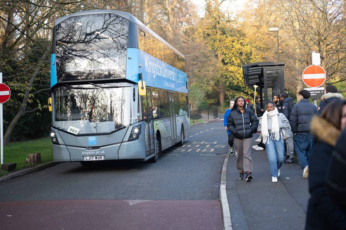 One of the Kingston University busses at a bus stop, with students walking past 