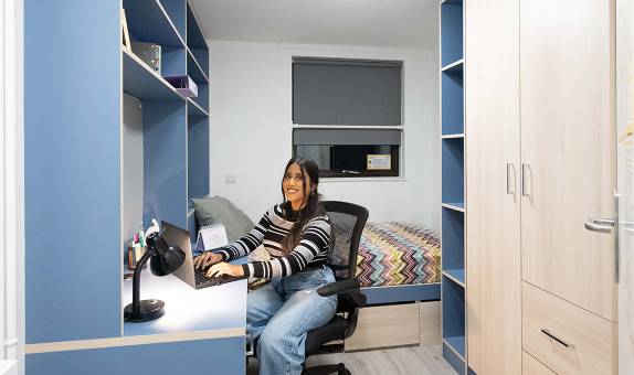 A female student sitting at her desk next to the bed in the premium en suite room at Chancellors Hall 