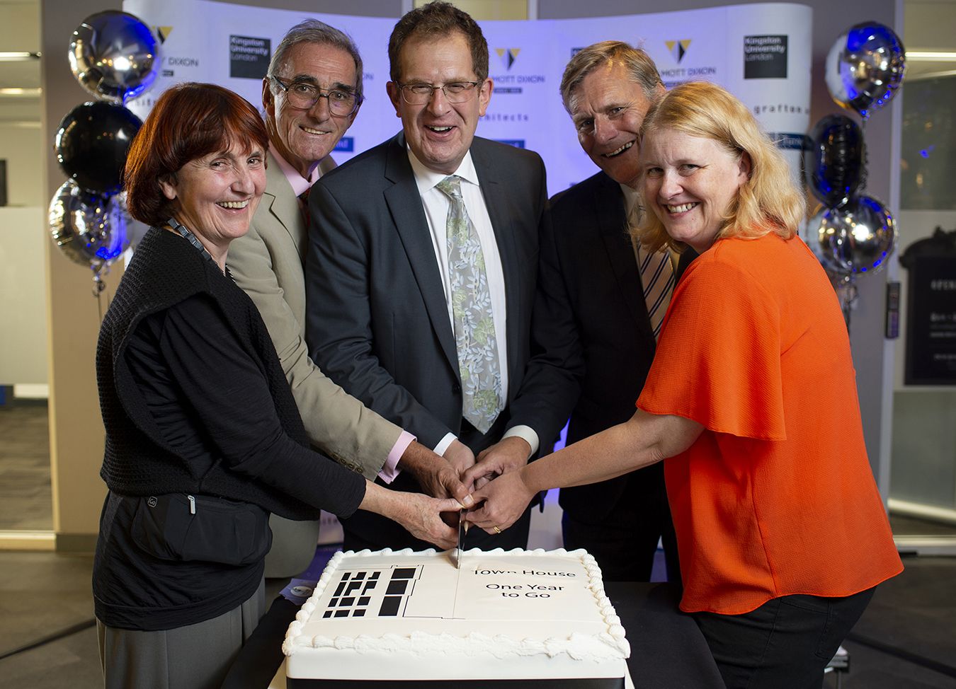 A photos of five people cutting a Town House cake