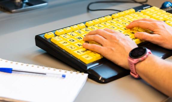 close up of hands typing on a high visibility keyboard 
