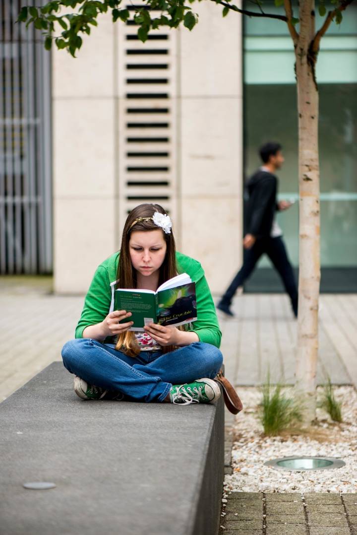 Student reading happily in the pleasant surroundings of Kingston University.
