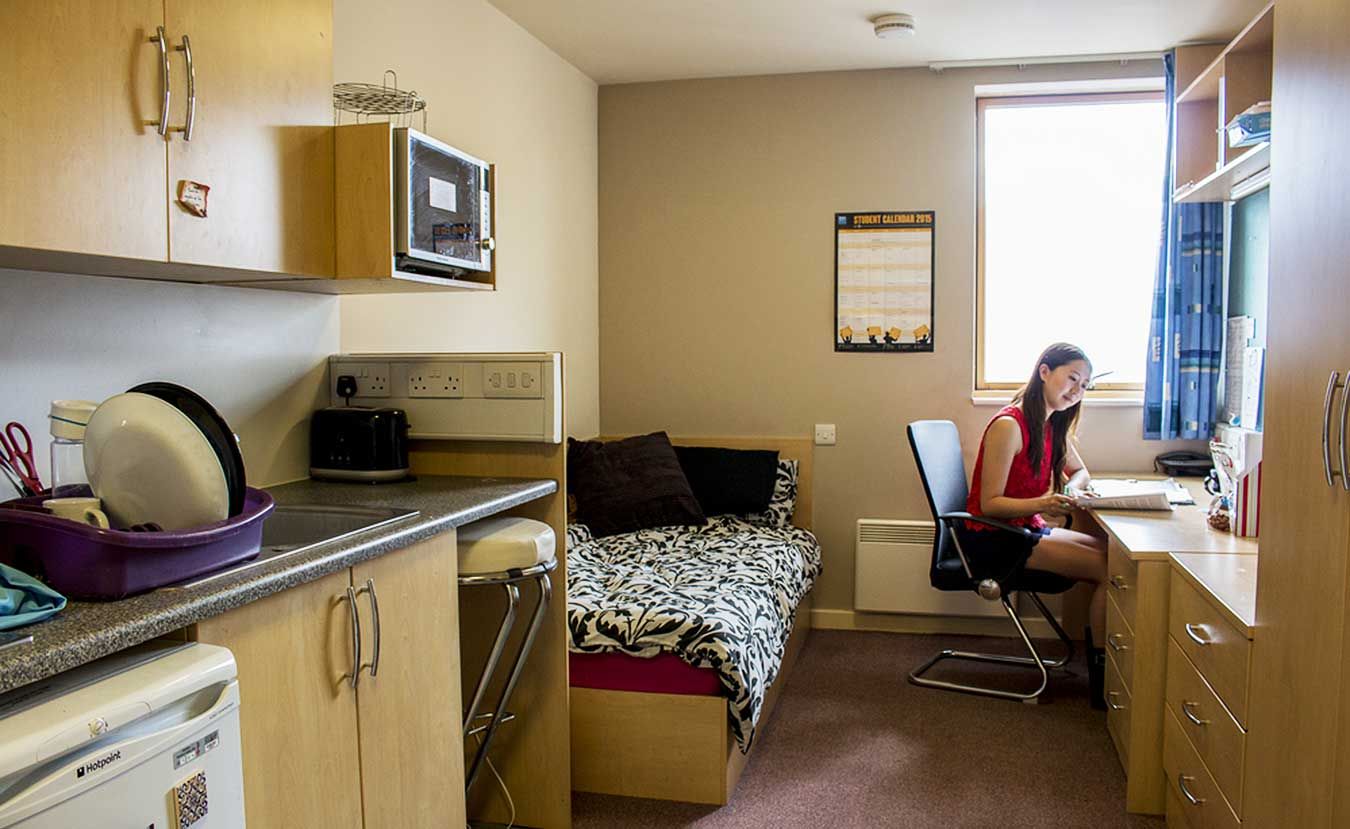 A picture of a Kingston University Hall of Residence room with a girl sitting at a desk.