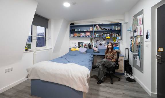 A female student sitting in their desk chair next to the bed in the premium en suite room