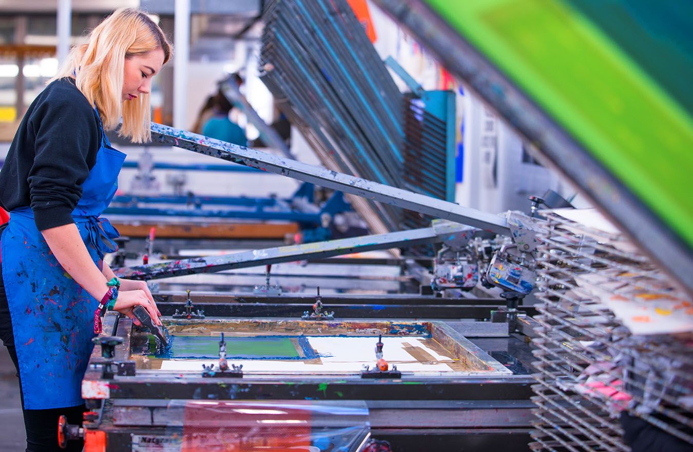 A photo of a Kingston School of Art student working on a screen printing machine.