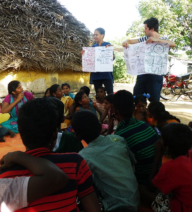 Picture of two staff members holding up pieces of paper while teaching Indian school children.