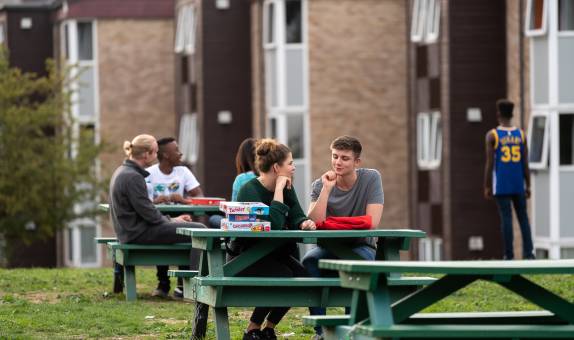 two students chatting on picnic benches outside halls of residence
