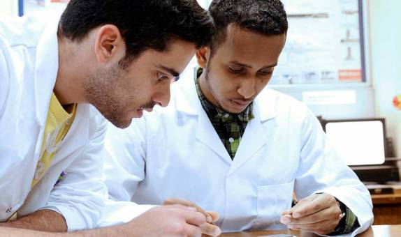 Two students in lab coats working together