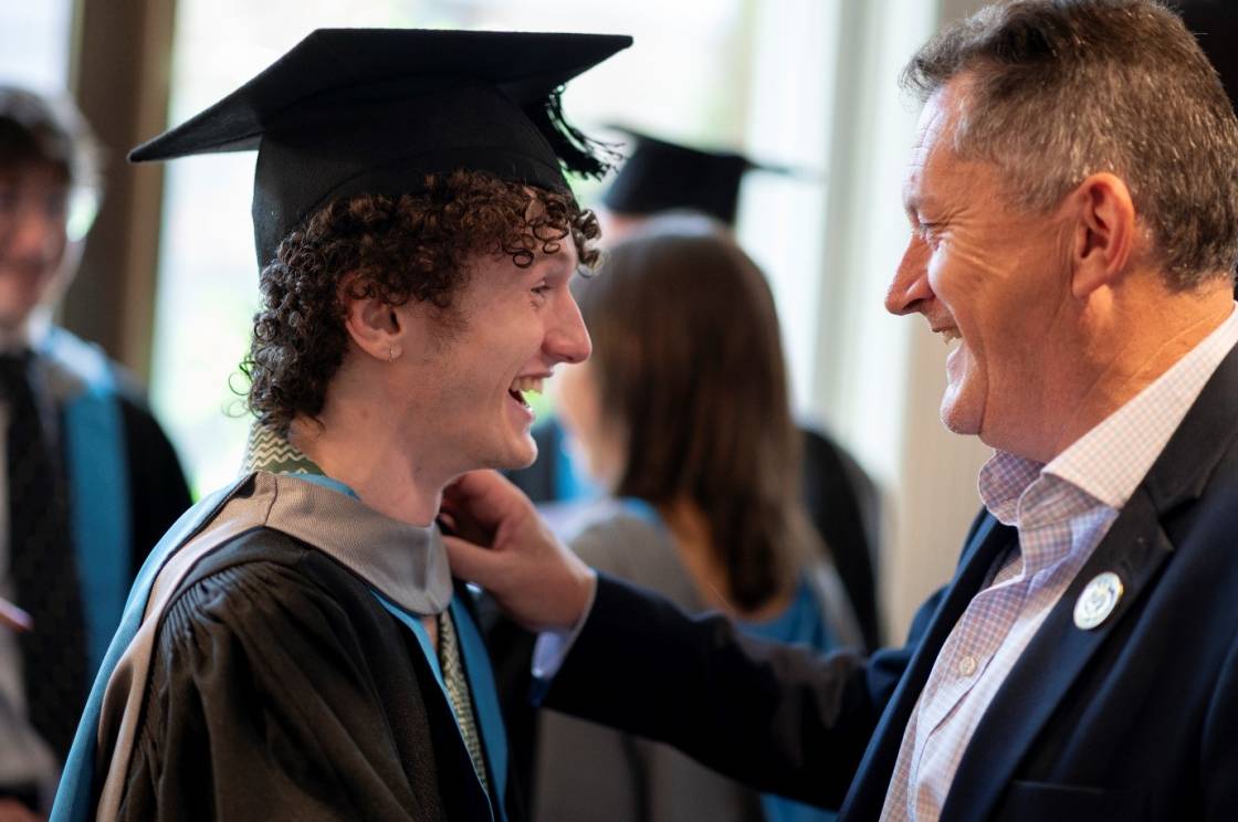 male graduate in robes talking and smiling with his dad in a suit