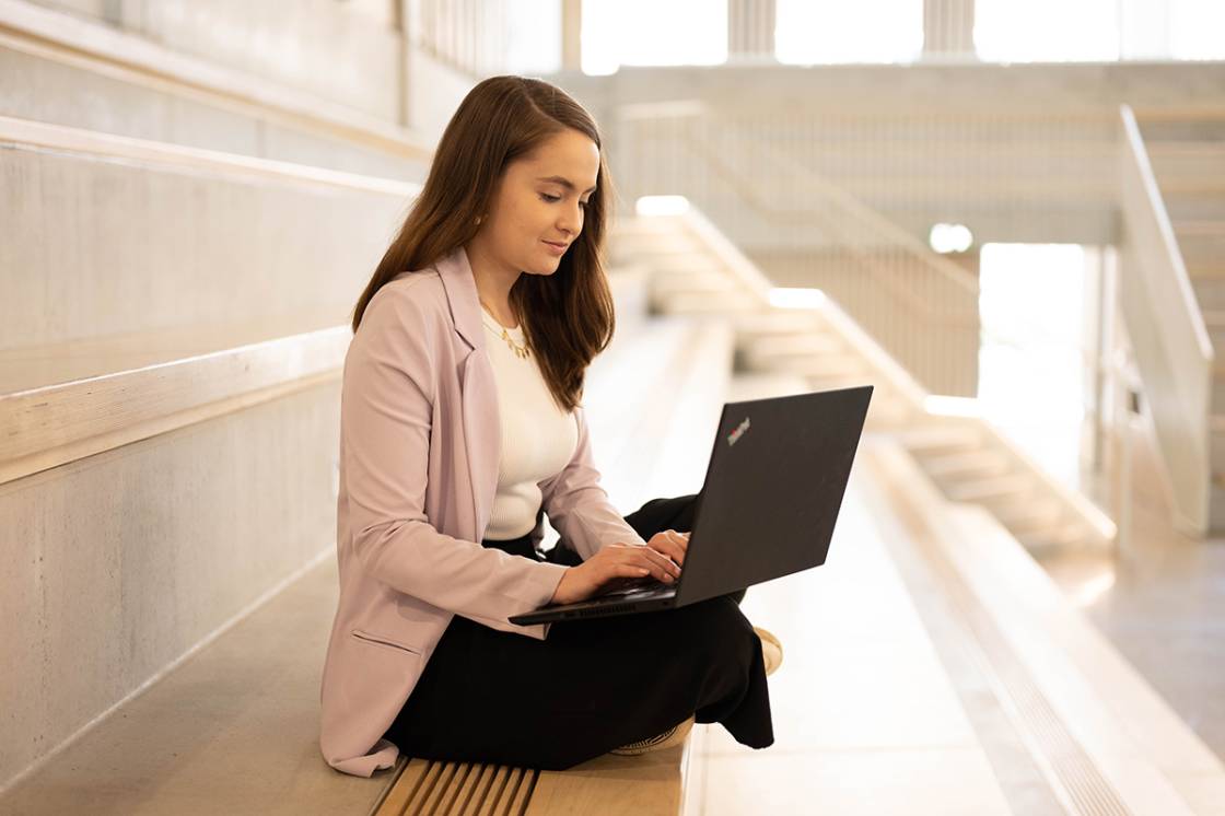 A woman sitting on the steps in the Town House auditorium, working on a laptop