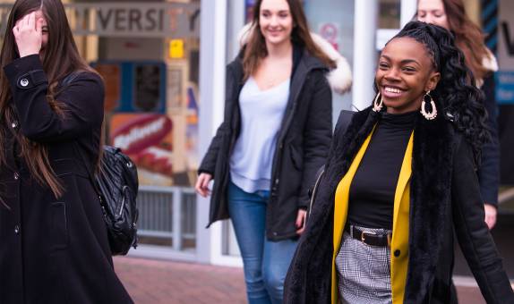 Three female KU students walking out the front entrance of Penrhyn Road campus and smiling
