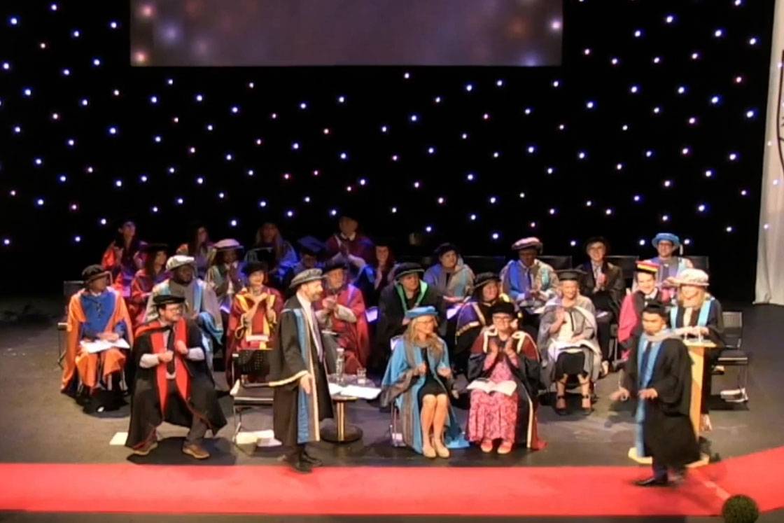 female graduate holds up certificate while dad takes a photo of her on his mobile phone