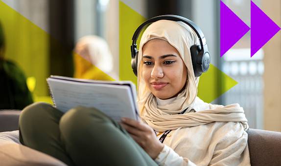 A female student wearing headphones reading from a notebook