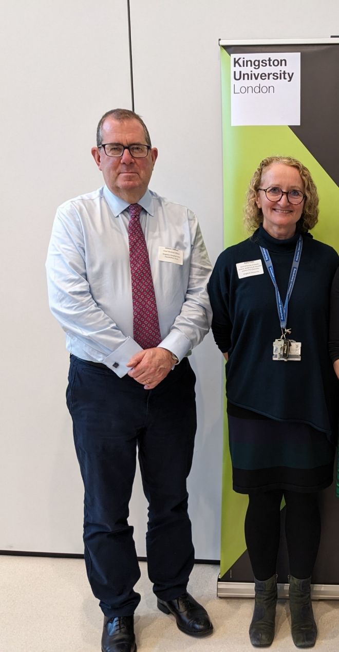 Two people standing with Kingston University logo in the background.