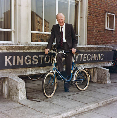 Len Lawley on a bicycle in front of Kingston Polytechnic sign